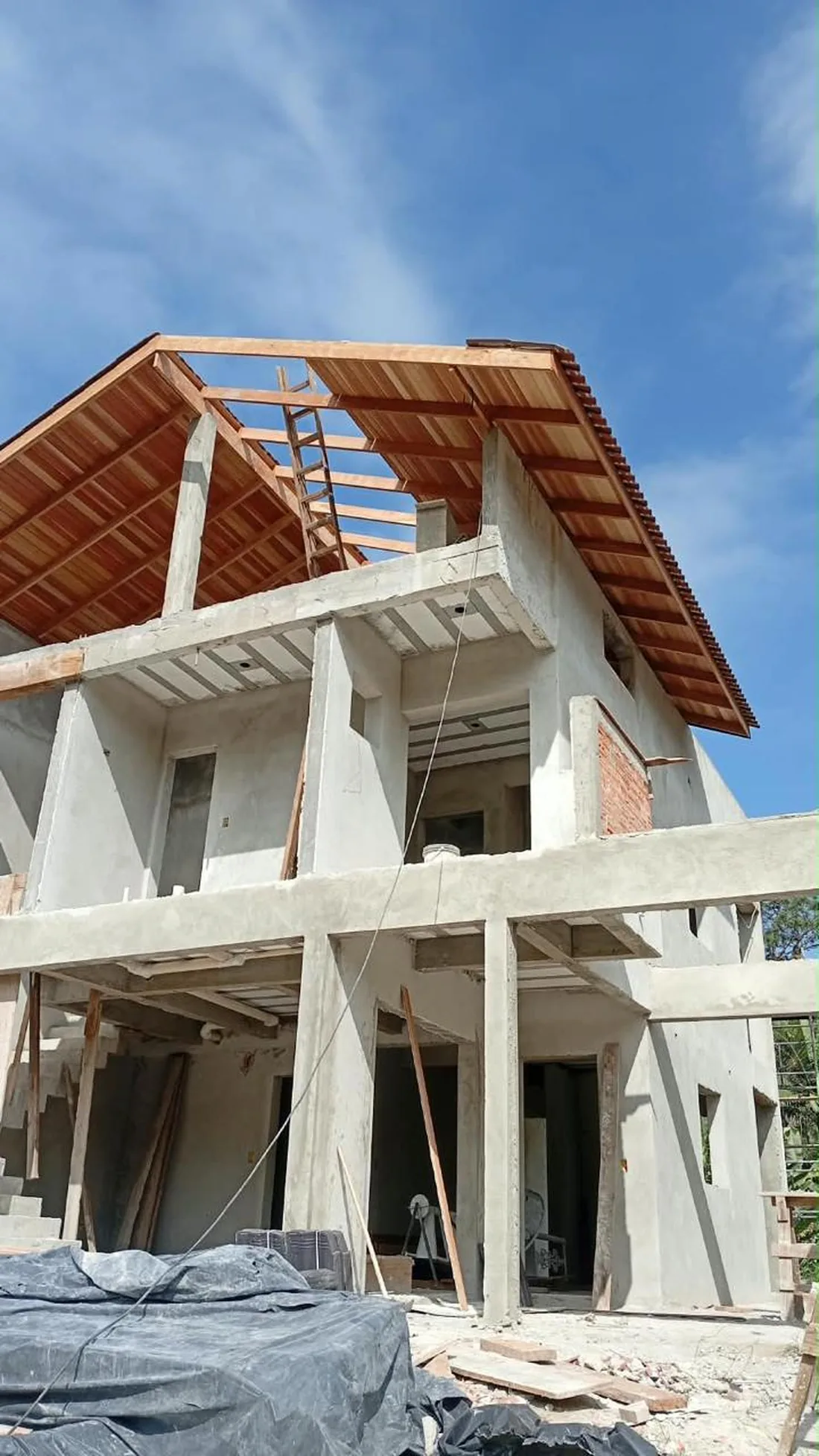 A mesma obra em execução, com estrutura de concreto concluída e estrutura de telhado em montagem.